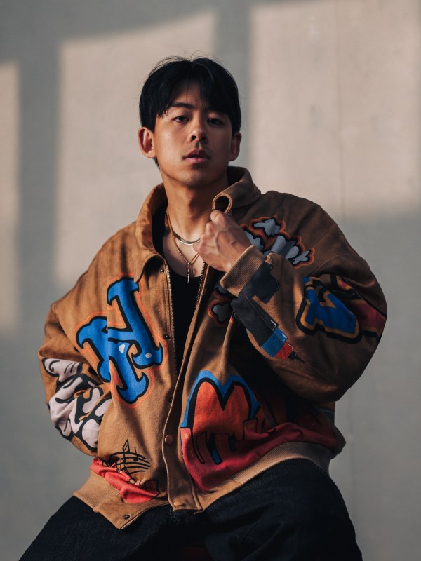 Editorial portrait in a graphic bomber jacket against concrete