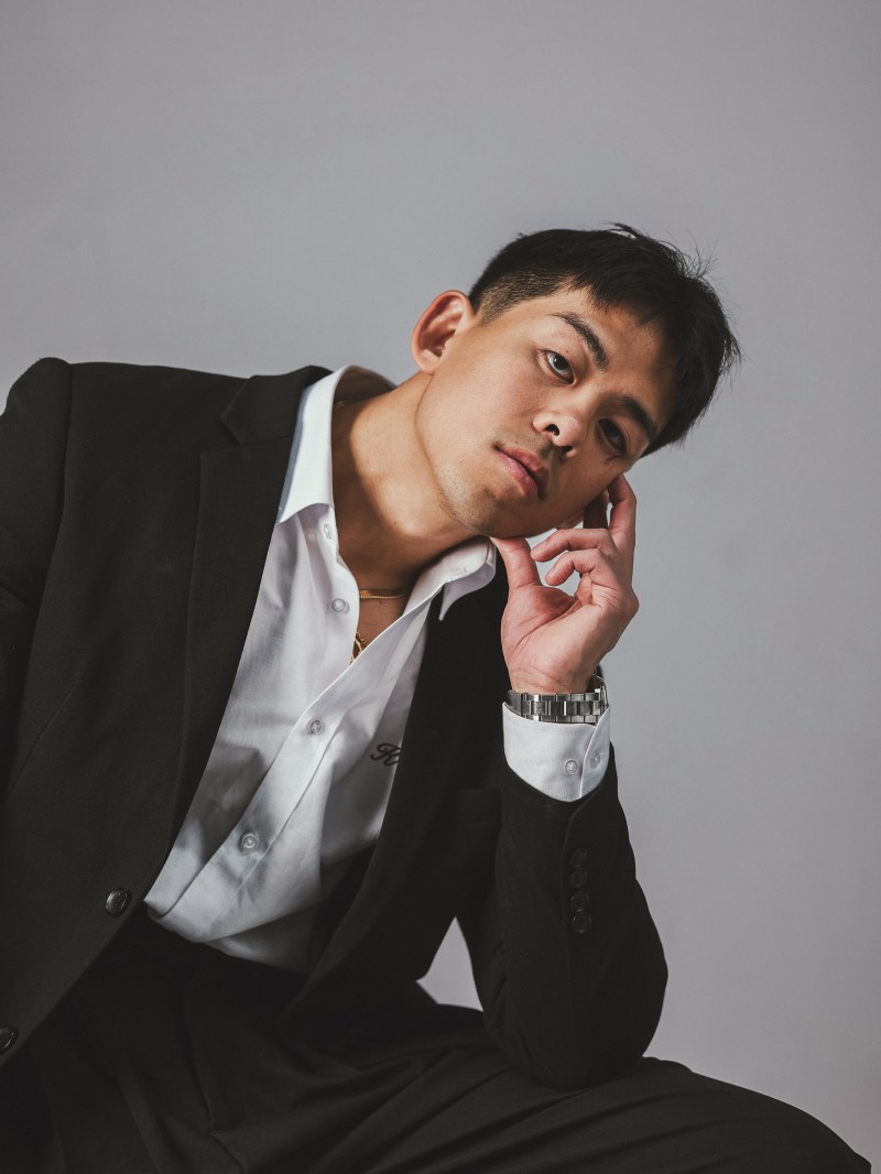 Seated studio portrait in a black suit against a grey backdrop